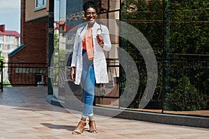 African american doctor female at lab coat, glasses with stethoscope posed outdoor against clinic