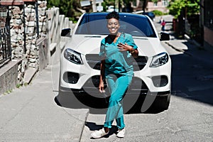 African american doctor female at lab coat with stethoscope posed outdoor against white suv car