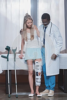 african american Doctor helping patient with leg brace stand