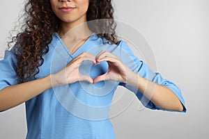 African-American doctor making heart with hands on light grey background, closeup