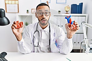 African american doctor man holding anatomical heart at the clinic clueless and confused expression