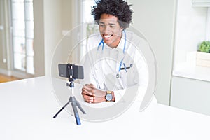 African American doctor man working and talking doing video conferece with smartphone with a happy face standing and smiling with