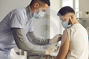 African-American doctor in medical face mask giving antiviral vaccine to young patient