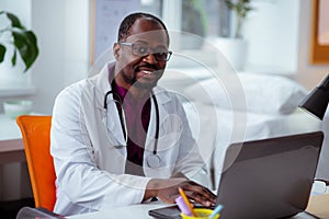 African-American doctor sitting at the table working on laptop