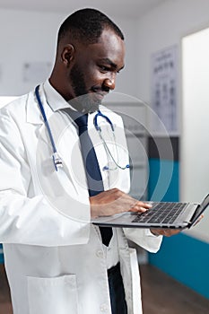 African american doctor with stethoscope typing medical expertise on laptop