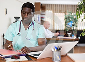 African american doctor therapist works at an computer, studying outpatient cards patients