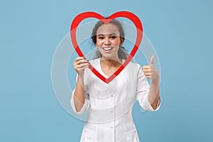 African american doctor woman isolated on blue background. Female doctor in white medical gown hold red wooden heart