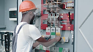 African american electrician in safety helmet and glasses checking voltage in switchgear while working at solar station