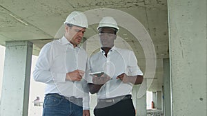 African american engineer and caucasine architect using digital tablet and wearing safety helmets at construction site