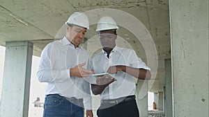 African american engineer and caucasine architect using digital tablet and wearing safety helmets at construction site