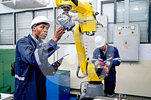 African American engineer or technician worker hold part of robotic arm and check the function of machine and co-worker support