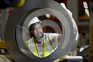 African American engineer worker is examining the stainless galvanized metal sheet roll inside the warehouse factory for roofing