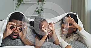 African american ethnic black mixed race family having fun indoor lying on sofa covered with blanket make funny faces