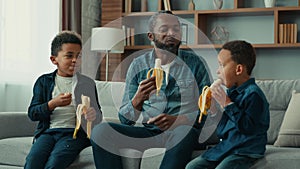 African American ethnic father dad man with two children little boys kids siblings sons eating bananas eat fruit tasty