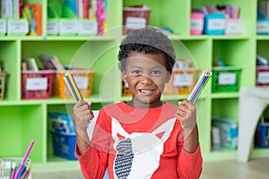 African American ethnicity kid holding group of color pencil smiling at library in kindergarten preschool classroom.education con