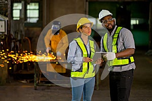 African American factory workers stand and discuss about their work in front of other worker use tools and generate sparks in the