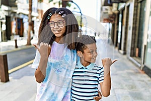 African american family of bother and sister standing at the street pointing thumb up to the side smiling happy with open mouth