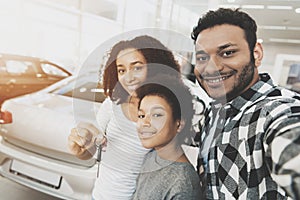 African american family at car dealership. Mother, father and son are taking selfie with keys for new car.