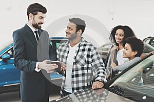 African american family at car dealership. Salesman is showing deatils for new car on tablet.