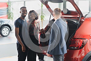 African american family at car dealership. Salesman is showing trunk of new red car