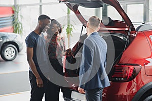 African american family at car dealership. Salesman is showing trunk of new red car