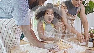 African American family with daughter thresh flour for cooking with father and mother together in the kitchen at home.