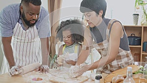 African American family with daughter thresh flour for cooking with father and mother together in the kitchen at home.