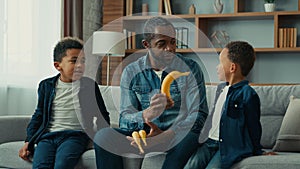 African American family at home single father man with two children boys dad talking with kids give bananas fruits
