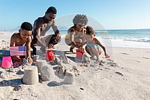 African american family making sandcastles together at beach on sunny day