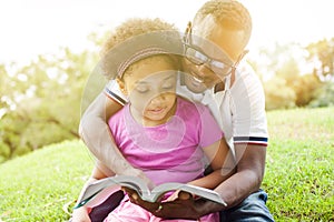 African American family reading a book together in the outdoor park.