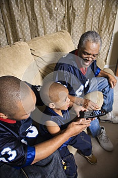 African-American family watching tv with boy holding remote.