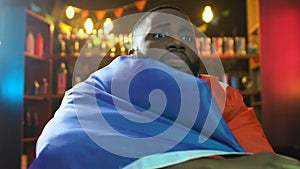 African-american fan with French flag watching match in pub, upset about defeat