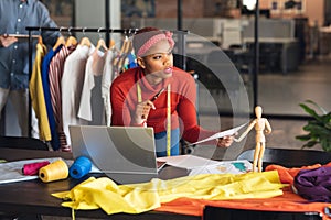 African american fashion designer with document and laptop looking away in studio office