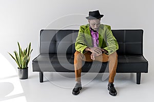 african american fashionable man in hat checking time while sitting photo