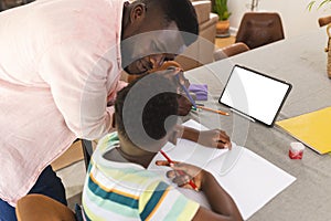 African American father assists a young son with homework at a table with copy space