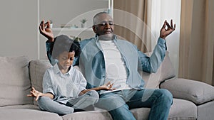 African american father and child sitting on sofa with closed eyes mature dad teaches little daughter to meditate manage