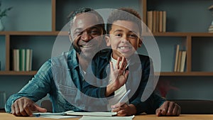 African American father dad with little son kid child boy schoolboy schoolchild schoolkid sit at table after homework