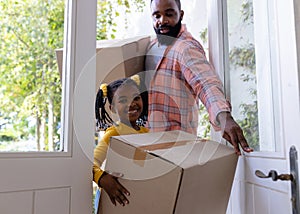 African american father and daughter with carboard boxes entering in new home