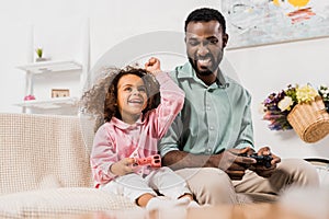 african american father and daughter playing video game with joysticks in