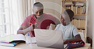 African american father helping son with homework while sitting with laptop and sanitizer bottle on