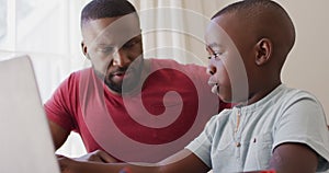 African american father helping son to use laptop while sitting at home