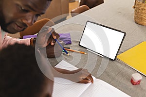 African American father helps a young son with homework, a blank tablet nearby with copy space