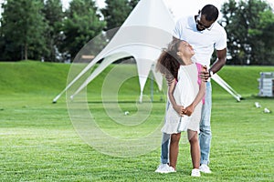 african american father hugging daughter with school bag