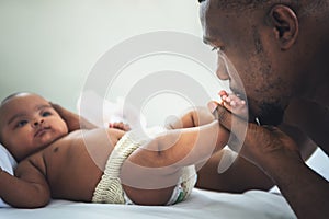 African American father kissing foot of his baby newborn daughter