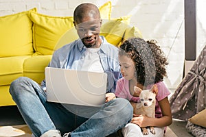 african american father and little daughter with dog using laptop together