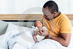 African American father looking and kissing and holding hands  his 12-day-old baby newborn