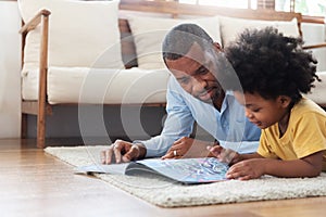 African American Father lying reading book on the floor with his son before traveling to work