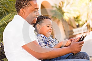 African American Father and Mixed Race Son Using Computer Tablet on Bench in Park