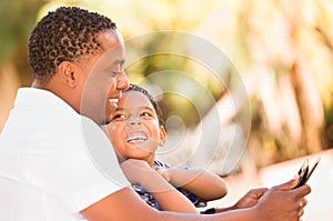 African American Father and Mixed Race Son Using Computer Tablet on Bench in Park