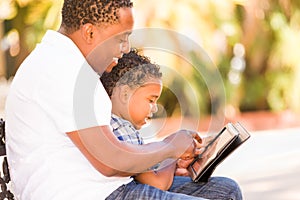 African American Father and Mixed Race Son Using Computer Tablet on Bench in Park